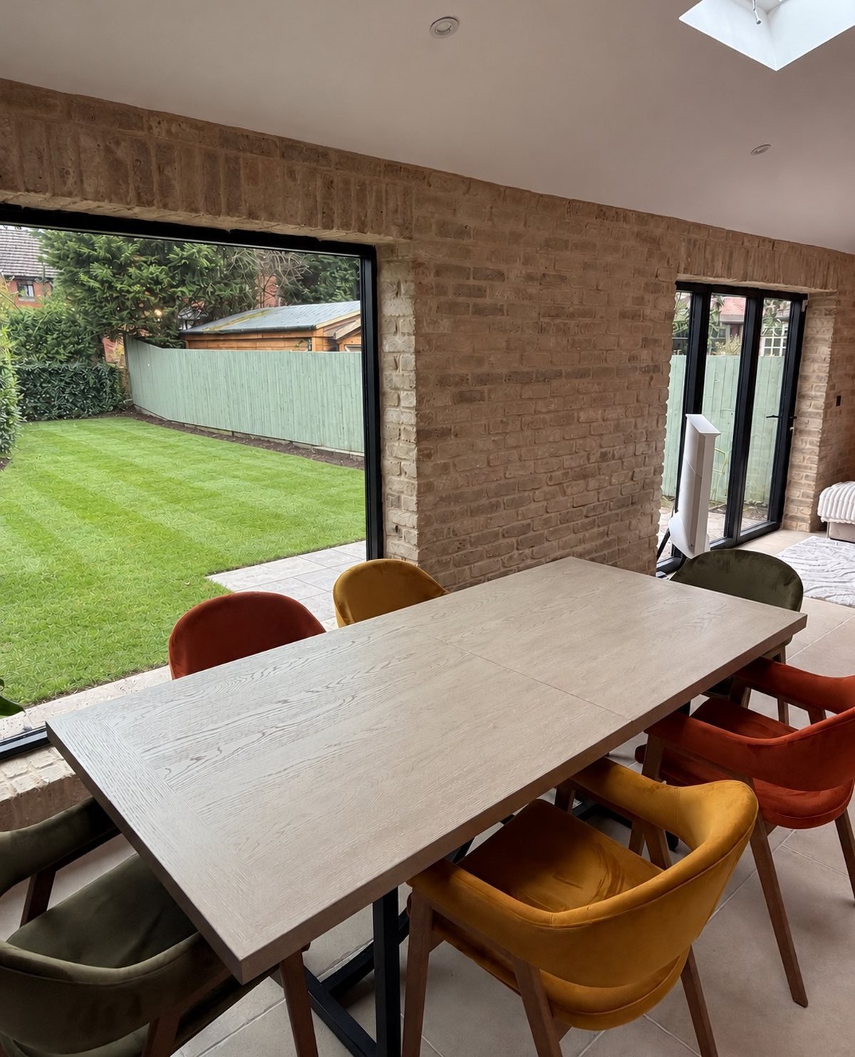 The same kitchen-diner finished: tiled floor and a buff brick slip feature wall around the garden window