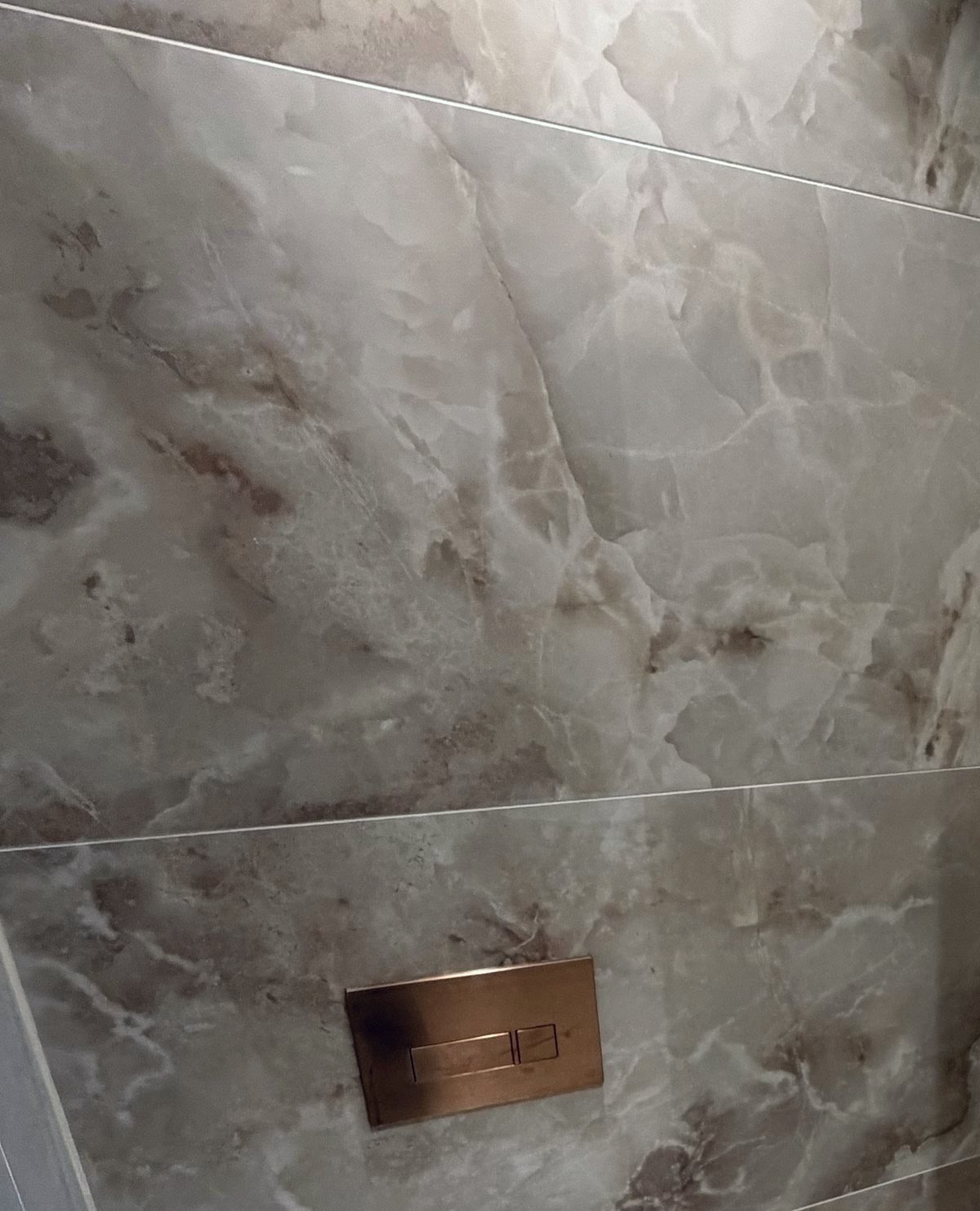 Close-up of marble-effect wall tiles with a copper flush plate