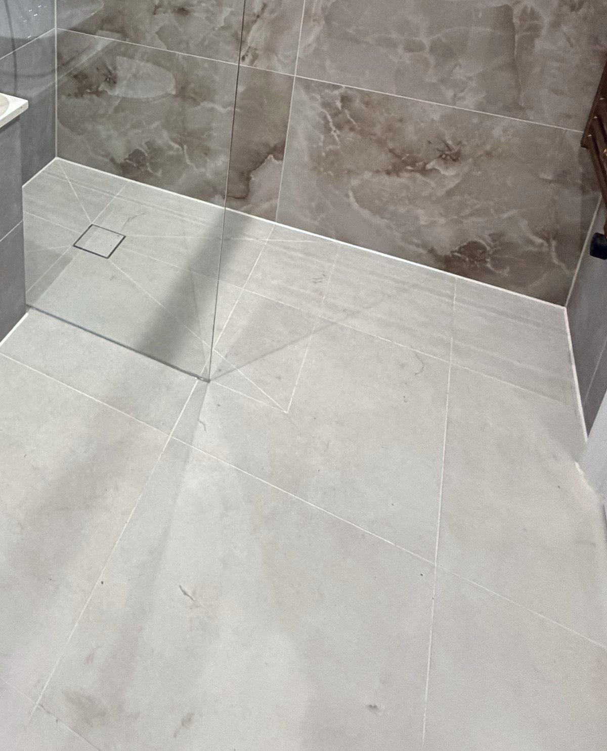 Large-format floor tiles running level into a walk-in shower with a square drain