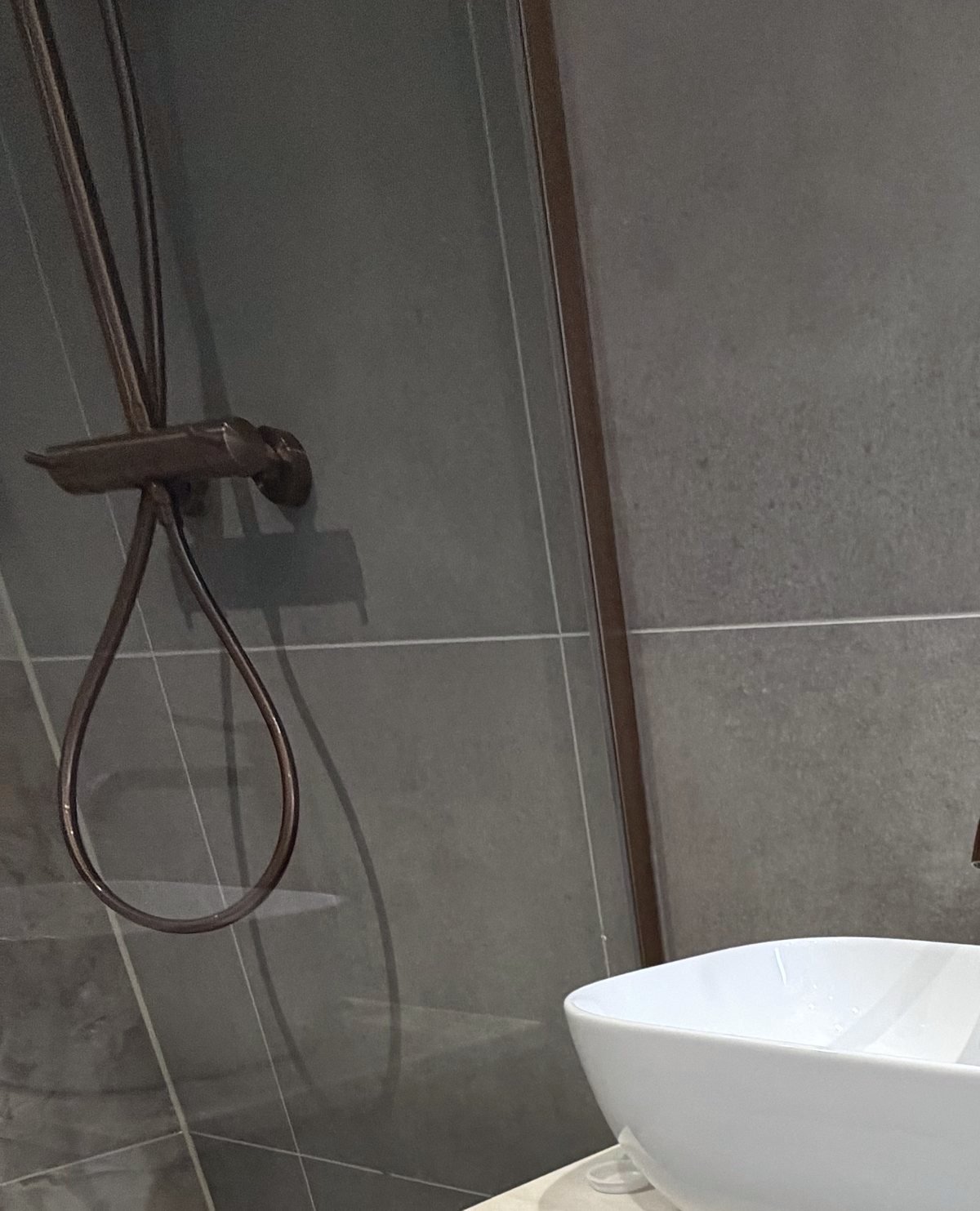 Copper shower mixer and hose against large grey wall tiles