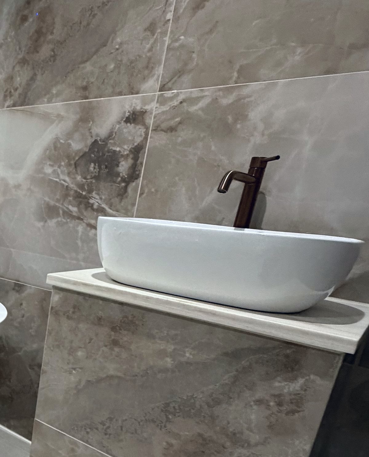 Close-up of a vessel basin and copper tap against marble-effect wall tiles