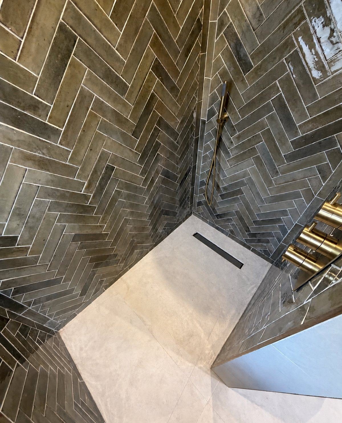 The same herringbone shower from above, with a stone-effect floor and linear drain