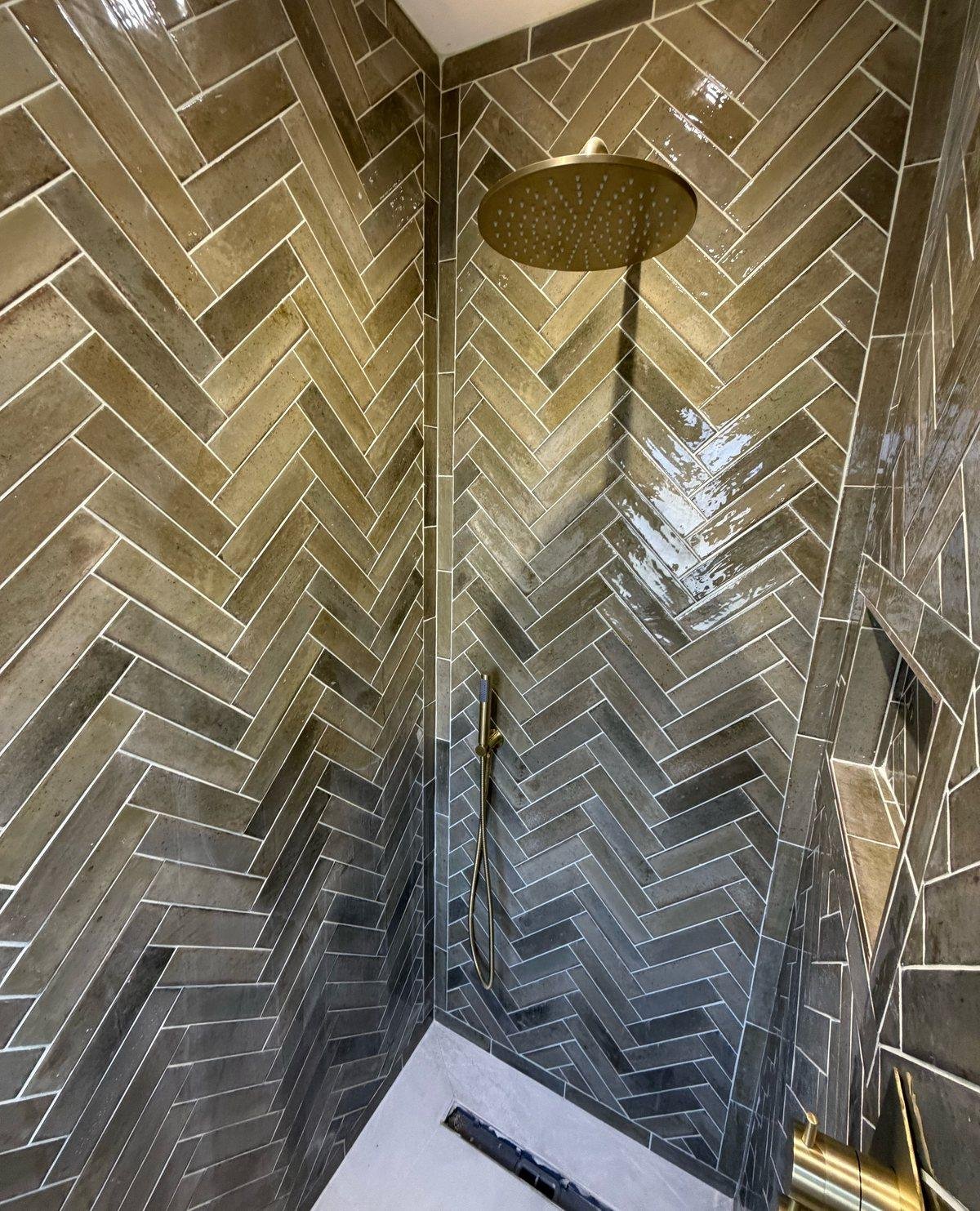 Walk-in shower tiled in khaki green herringbone with a brass rain shower head