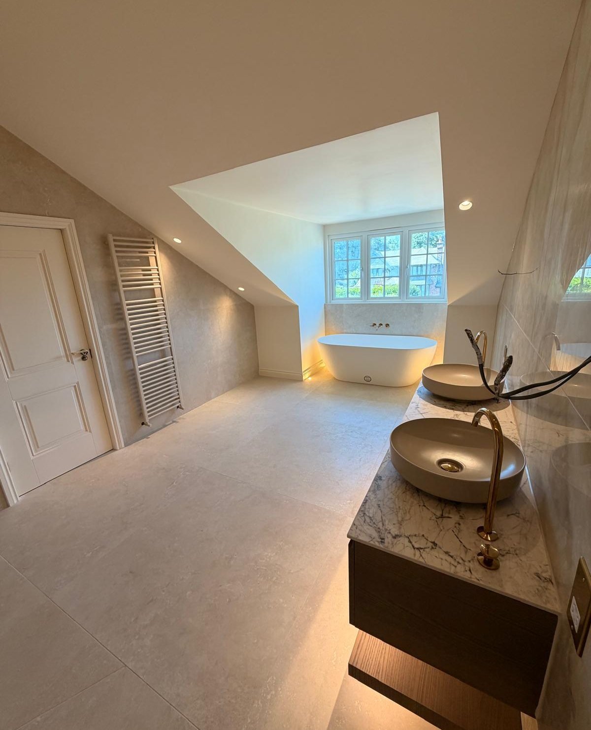 The same loft bathroom finished: freestanding bath under the dormer and marble-effect walls