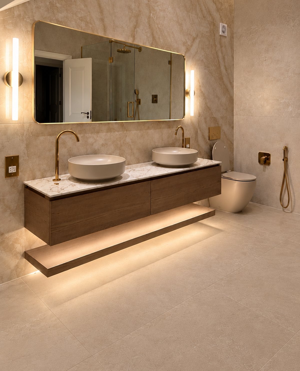 Double vanity with brass taps and a lit mirror against marble-effect wall tiles