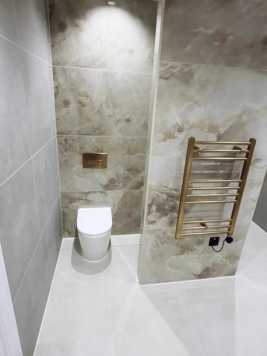 Same WC wall finished in marble-effect tiles with wall-hung WC and brass towel rail