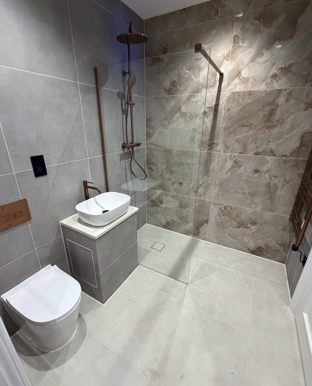 Finished wet room corner: wall-hung WC, vanity and walk-in shower in marble-effect tiles with copper fittings