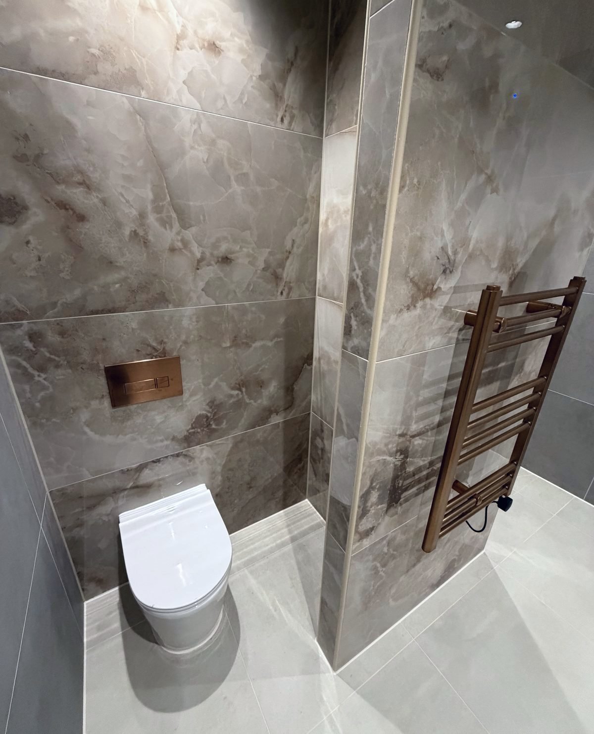 The same partition finished in marble-effect tiles, with a wall-hung WC and copper towel rail